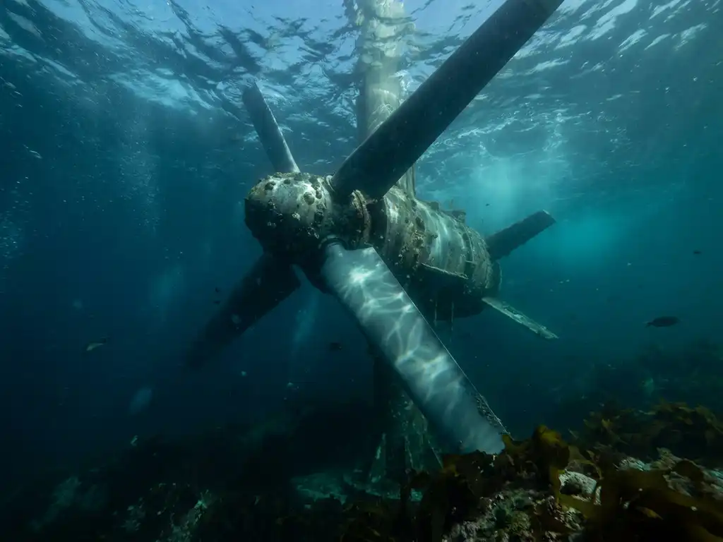 Tidal turbine submerged underwater with steel blades turning against ocean currents, rocky seabed below, blue-green light filtering from surface.